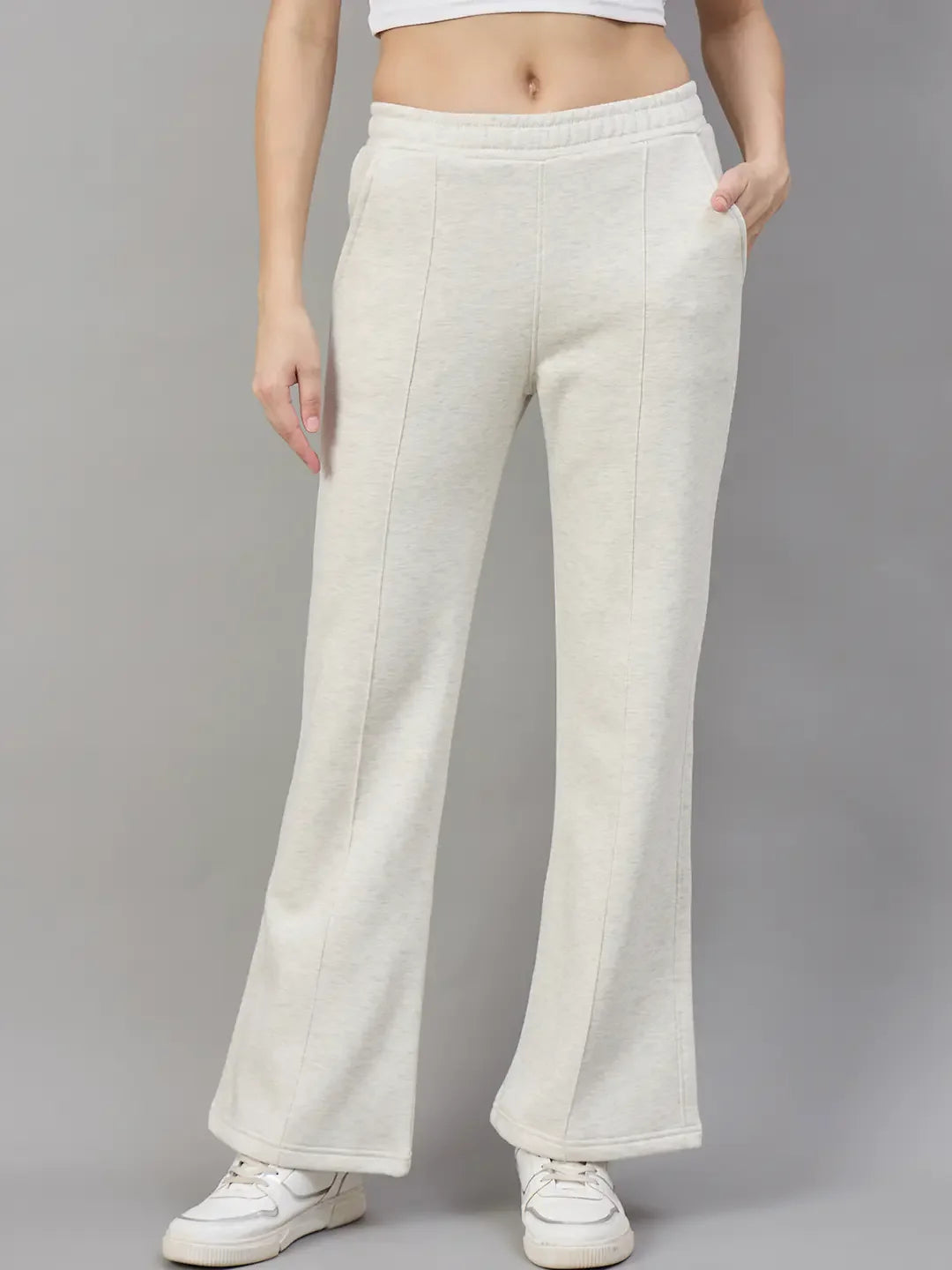 Model wears 98degreenorth Womens Flared Sweatpants in Ecru Off White with white sneakers and a crop top, on gray backdrop.