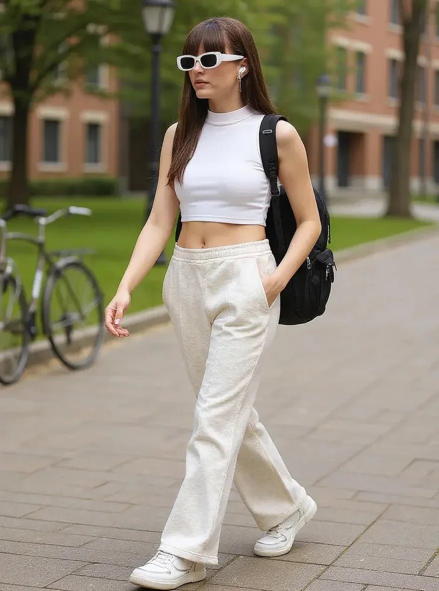 A woman in white sunglasses, a crop top, and 98degreenorth Ecru Flared Sweatpants walks outside with a black backpack.