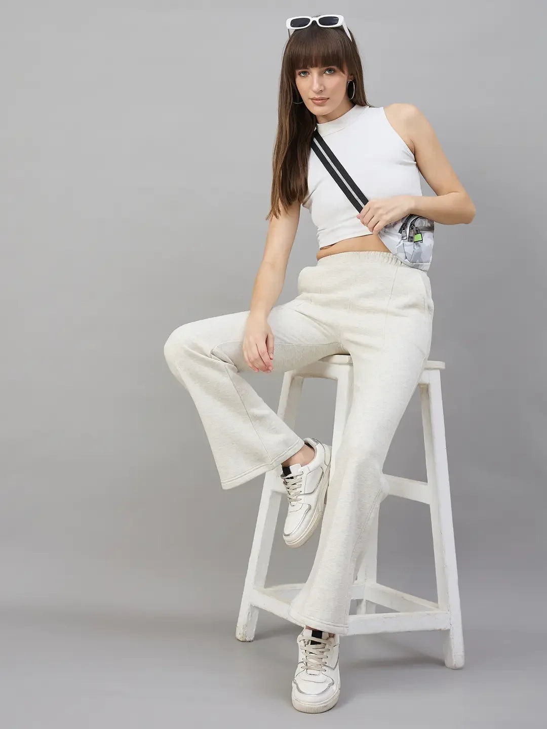 Woman in 98degreenorth Women’s Flared Sweatpants in Ecru Off White sits on a wooden ladder, sneakers and sunglasses on.