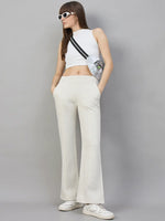 Woman in 98degreenorth’s ecru flared sweatpants, crop top, sneakers, crossbody bag & sunglasses on gray backdrop.