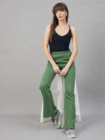 A woman wears 98degreenorth Women’s Flared Sweatpants in Hunter Green, seated on a white stool against a grey background.