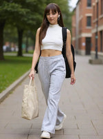 A young woman in 98degreenorth’s Women’s Flared Sweatpants in Light Grey walks outside carrying a tote bag and backpack.