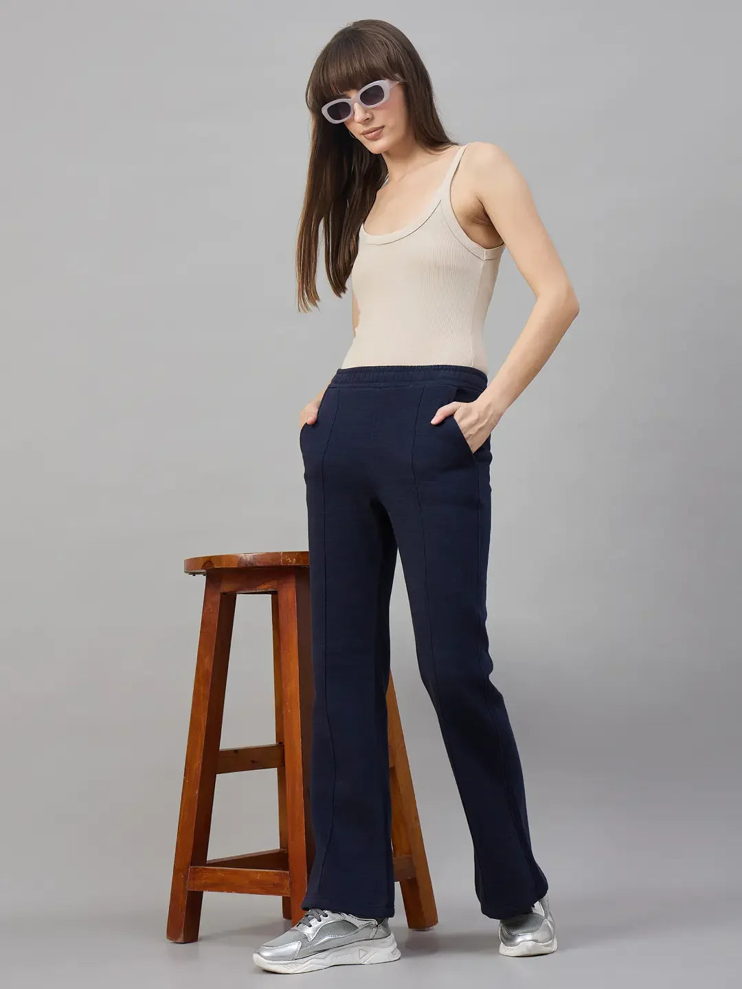 Woman in a beige tank top and 98degreenorth Womens Flared Sweatpants in Navy Melange stands by a wooden stool.