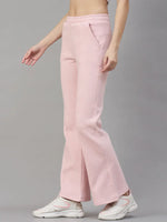 Woman in 98degreenorth Women’s Flared Sweatpants in Pink Melange, styled with white sneakers, poses by a gray wall.