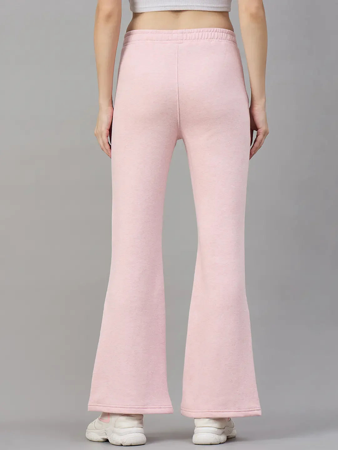 Model in 98degreenorth Women’s Flared Sweatpants in Pink Melange, shown from the back with white sneakers on gray background.