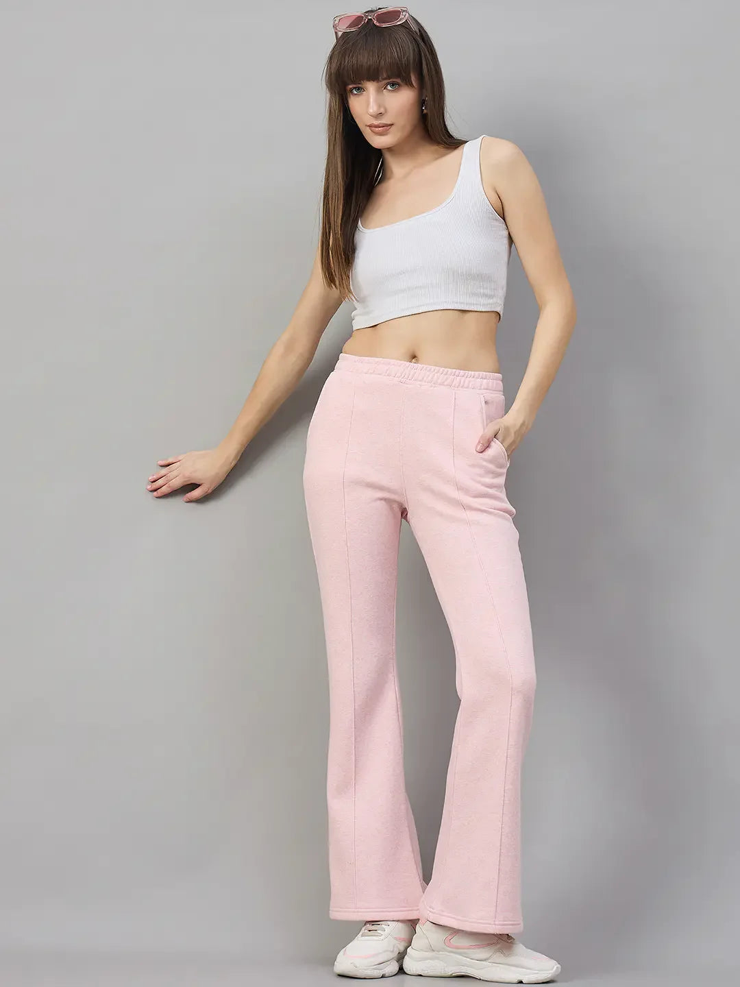 Woman in 98degreenorth Pink Melange Flared Sweatpants poses in white crop top, sneakers, and sunglasses.