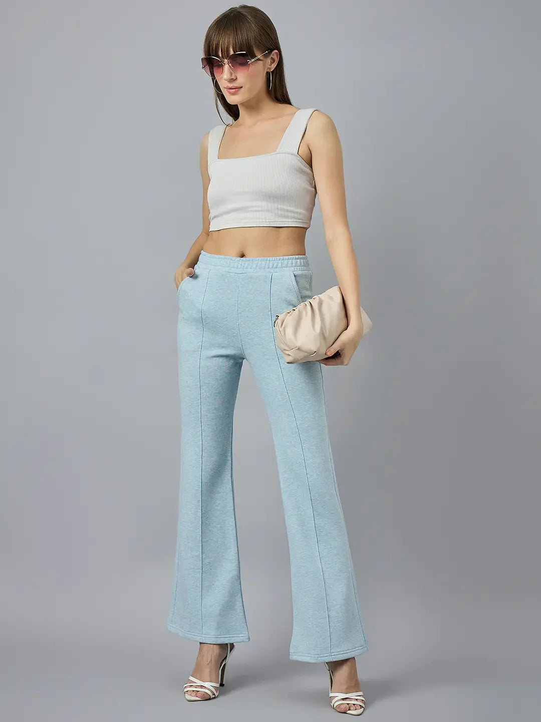 Woman in 98degreenorth Women’s Flared Sweatpants in Sky Melange, paired with a white crop top and beige clutch.