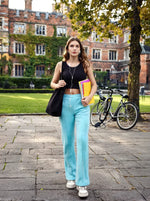 A young woman in 98degreenorth turquoise blue flared sweatpants walks on campus, books in hand, bikes and brick building behind.