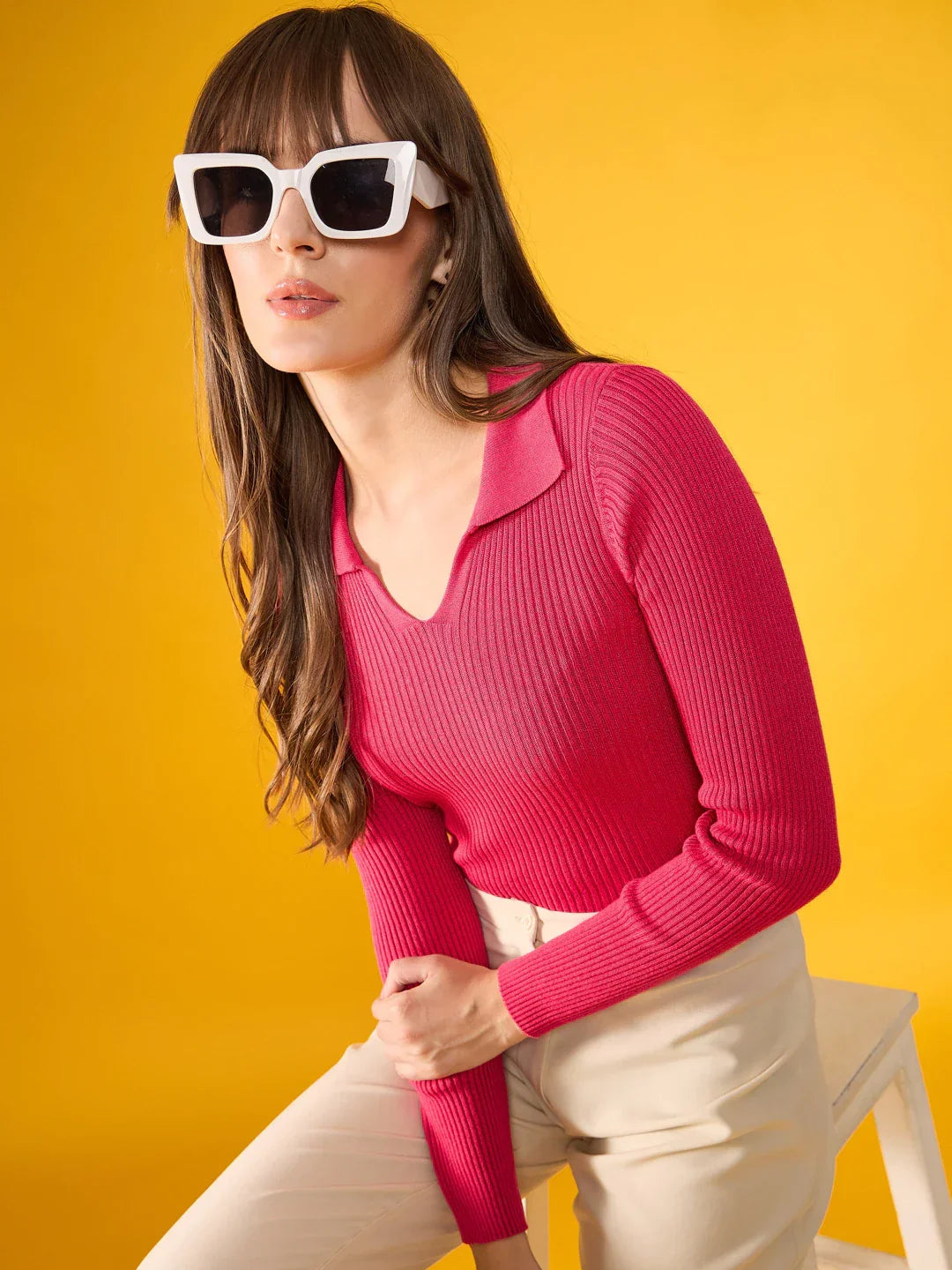 Woman in white sunglasses wears 98degreenorth fuchsia pink ribbed collar sweater against a bright yellow background.