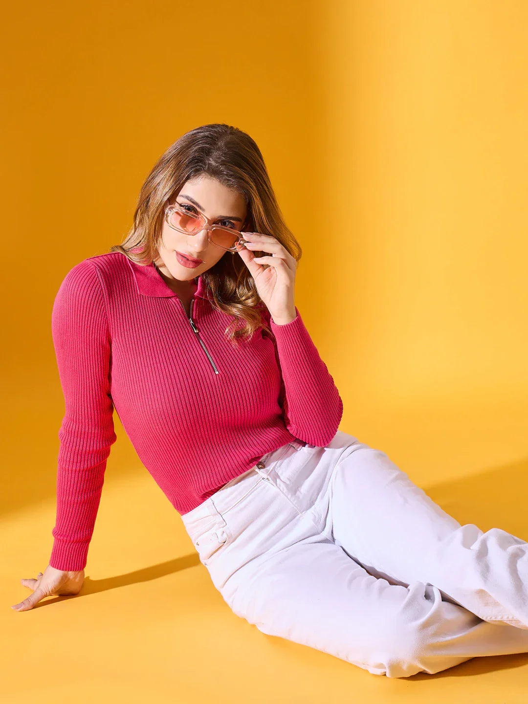 Woman wears 98degreenorth Fuchsia Ribbed Zipper Sweater, slim fit, sitting on floor with white pants and yellow background.