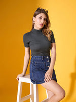 Woman wears 98degreenorth's green ribbed turtle neck slim fit sweater, seated on a stool against a yellow background.