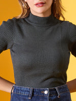 Woman wears 98degreenorth green ribbed slim fit turtleneck sweater with high-waisted jeans, yellow background.