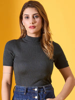 Woman in a 98degreenorth green ribbed turtle neck sweater and jeans, standing against a yellow background.