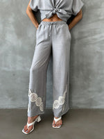 Woman in 98degreenorth grey wide leg linen pants with crochet detail and drawstring waist, standing by a gray wall.