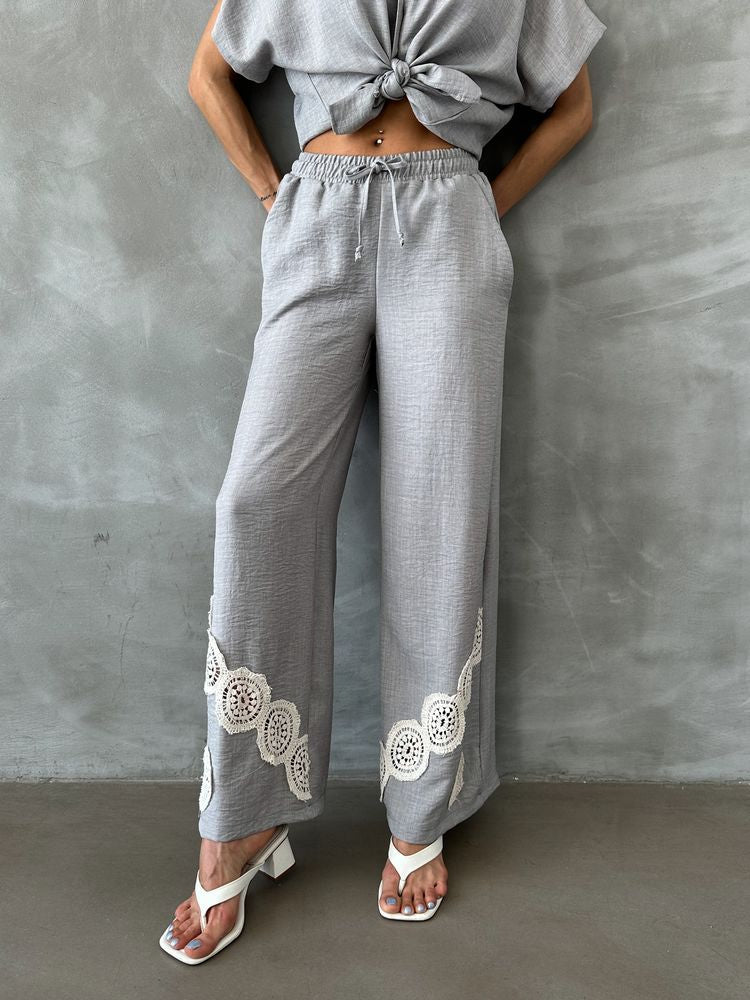 Woman in 98degreenorth grey wide leg linen pants with crochet detail and drawstring waist, standing by a gray wall.