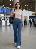 Woman in a beige hoodie and 98degreenorth Indigo Blue Flared Bootcut Lounge Pants walks by airport flight boards.