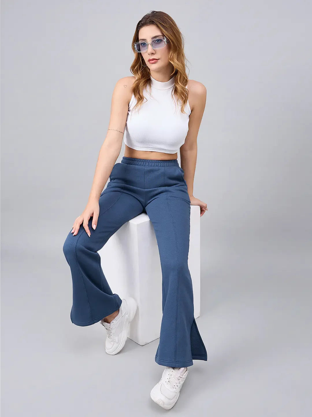 Woman in a white crop top and 98degreenorth Women’s Indigo Blue Bootcut Sweatpants sits on a white block.
