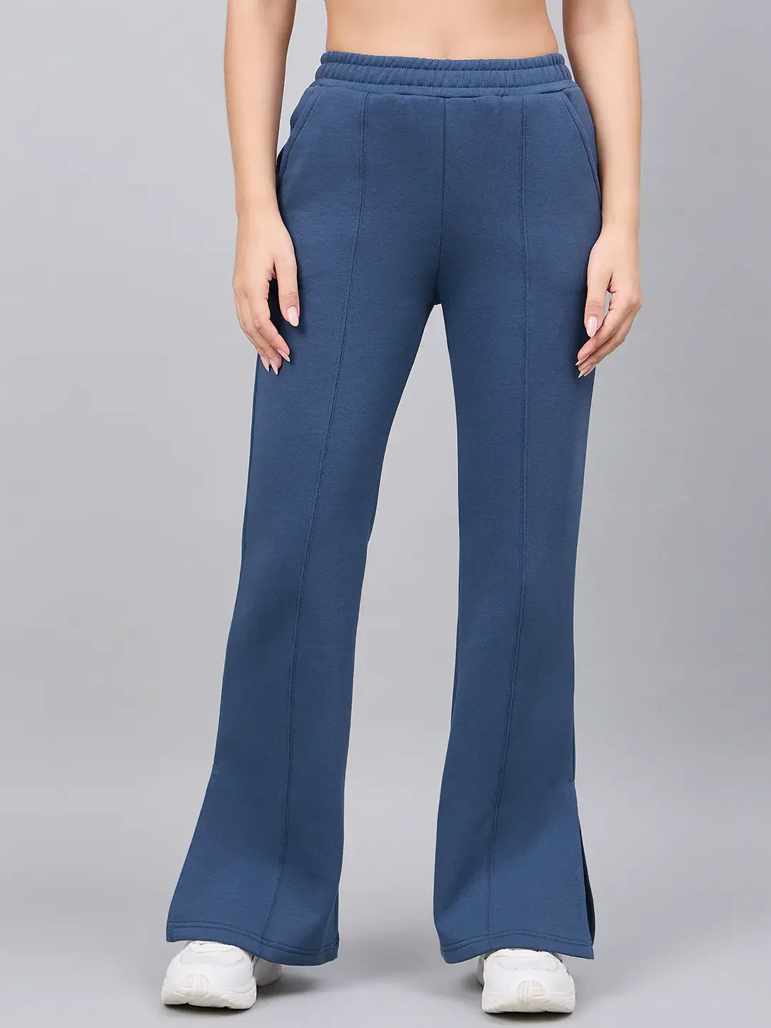 A woman wears 98degreenorth’s Indigo Blue Bootcut Sweatpants with white sneakers against a plain gray background.