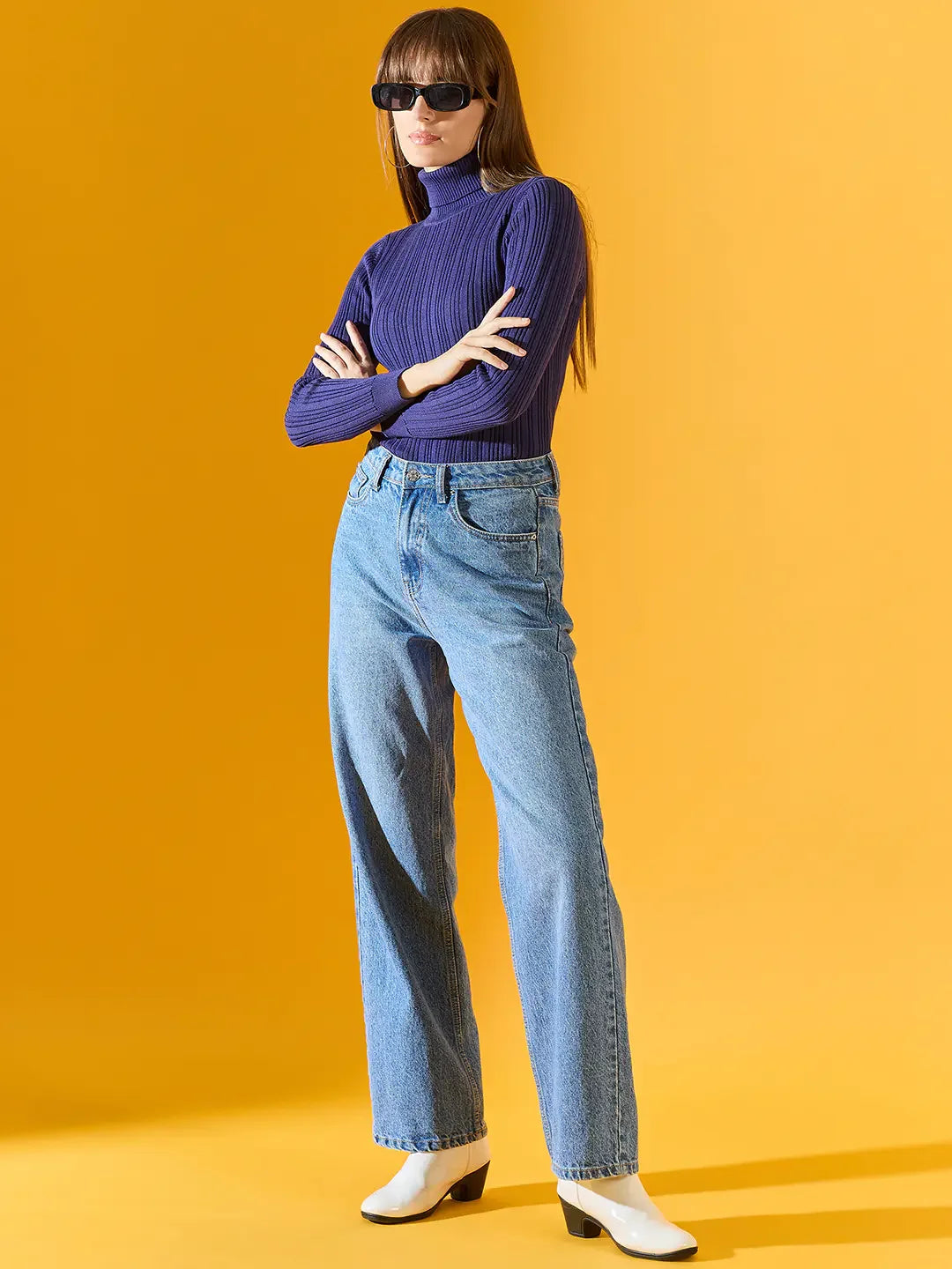 Woman in sunglasses wears 98degreenorth Women’s Ink Blue Ribbed Turtleneck Sweater with blue jeans and white boots.