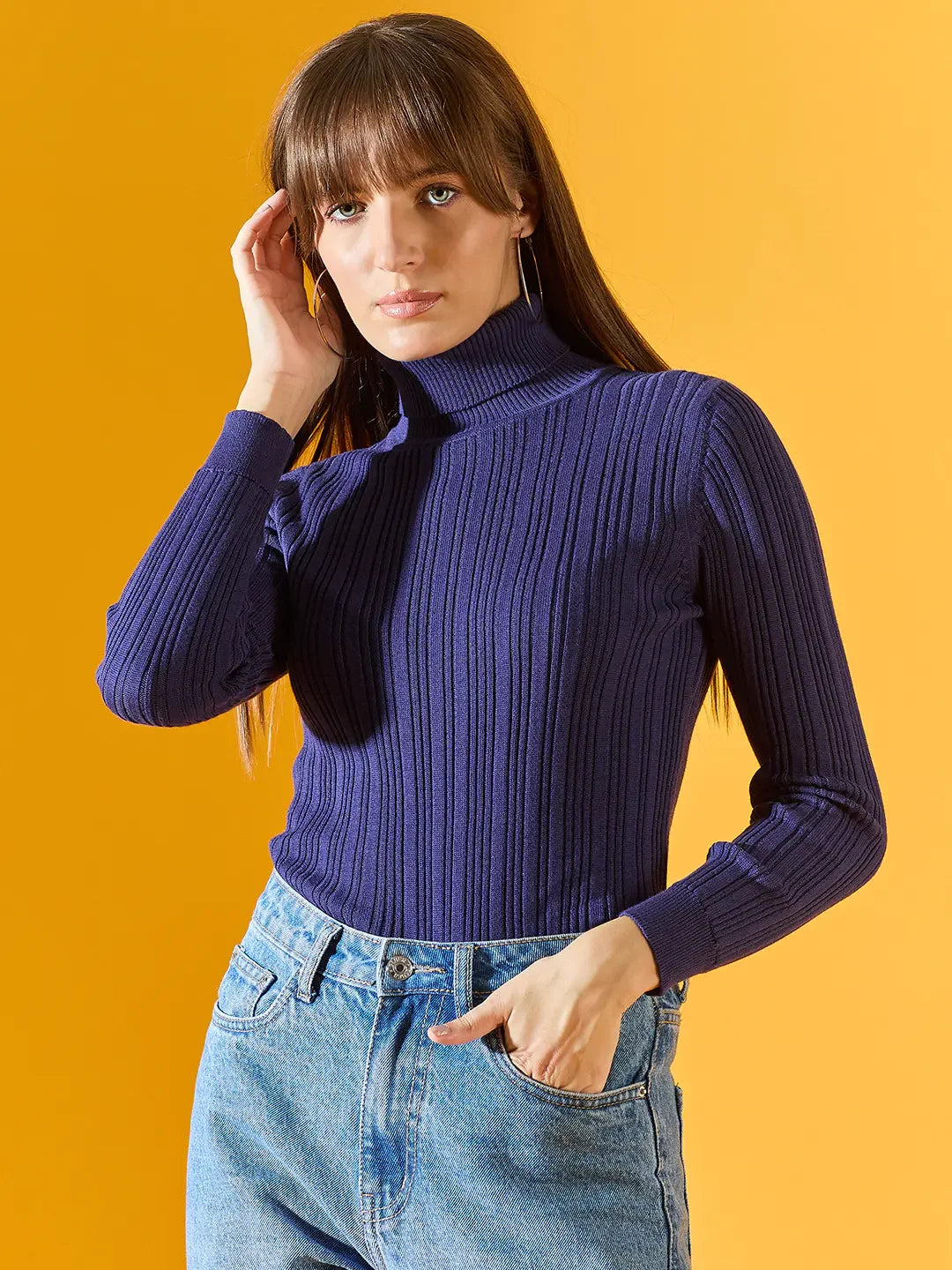 Woman in a 98degreenorth Ink Blue Ribbed Turtleneck Sweater poses against a solid yellow background.
