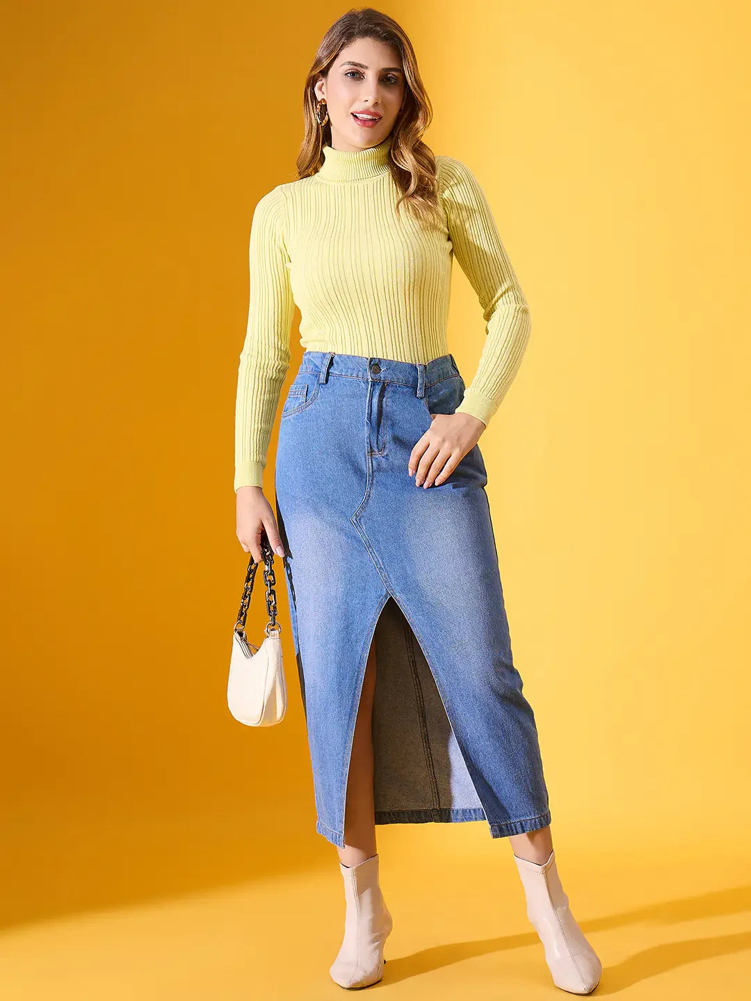 A woman wears the 98degreenorth Lemon Ribbed Turtleneck Sweater with a denim skirt and white boots in a yellow setting.