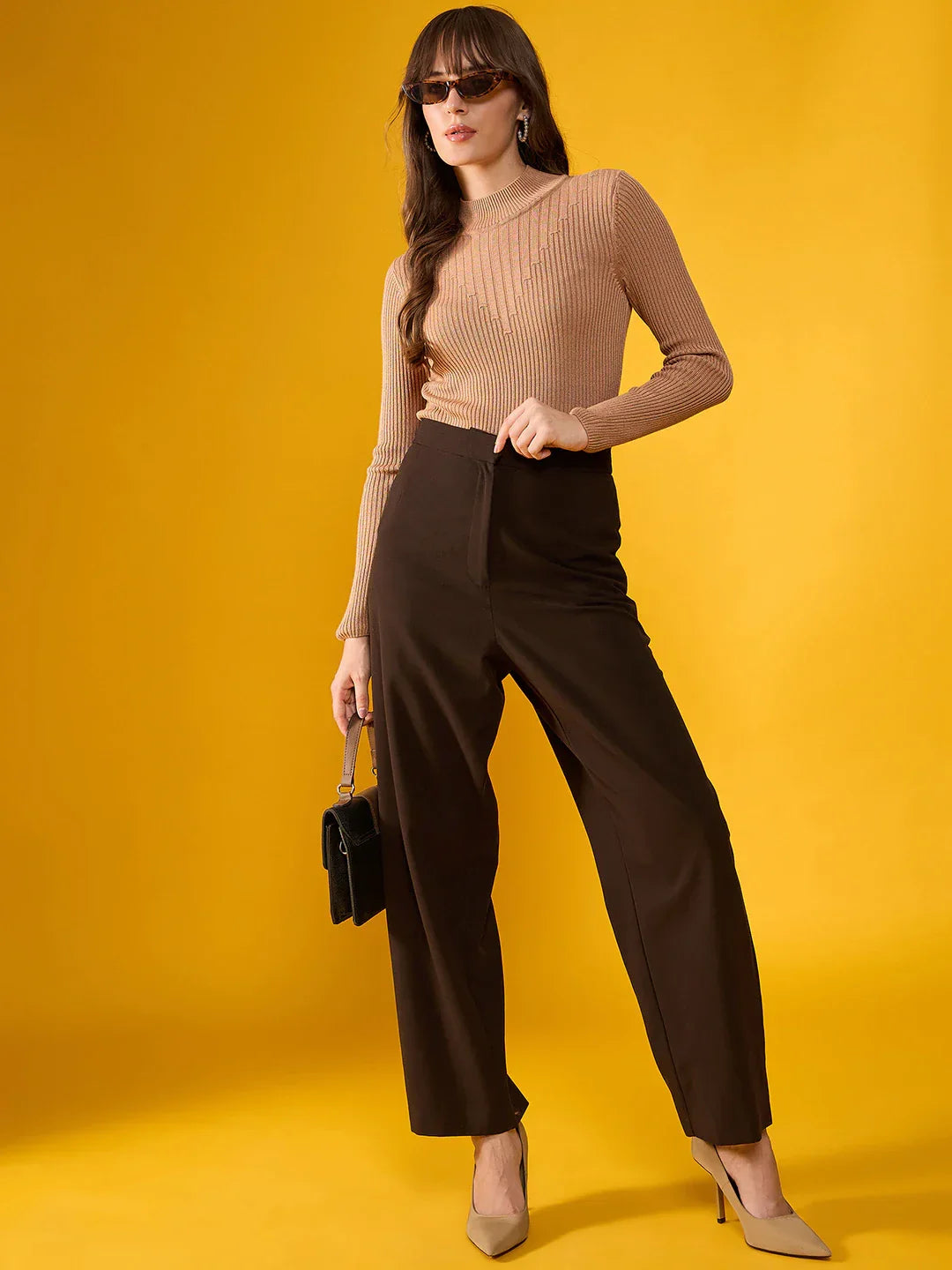 Woman in sunglasses wears 98degreenorth’s light camel ribbed turtleneck sweater and brown pants, holding a black bag.