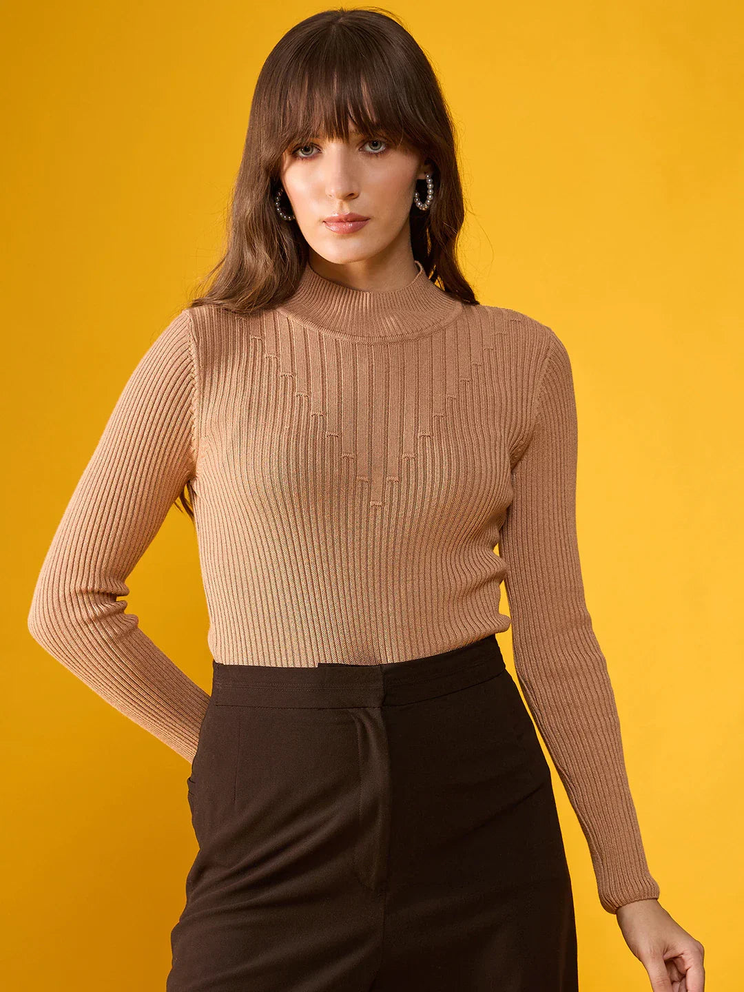 Woman in a 98degreenorth Light Camel Ribbed Turtle Neck Slim Fit Sweater and black pants stands against a yellow background.