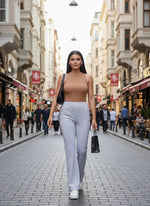 Woman in a sleeveless brown top and 98degreenorth Women’s Light Grey Flared Bootcut Trousers walks with a black bag.