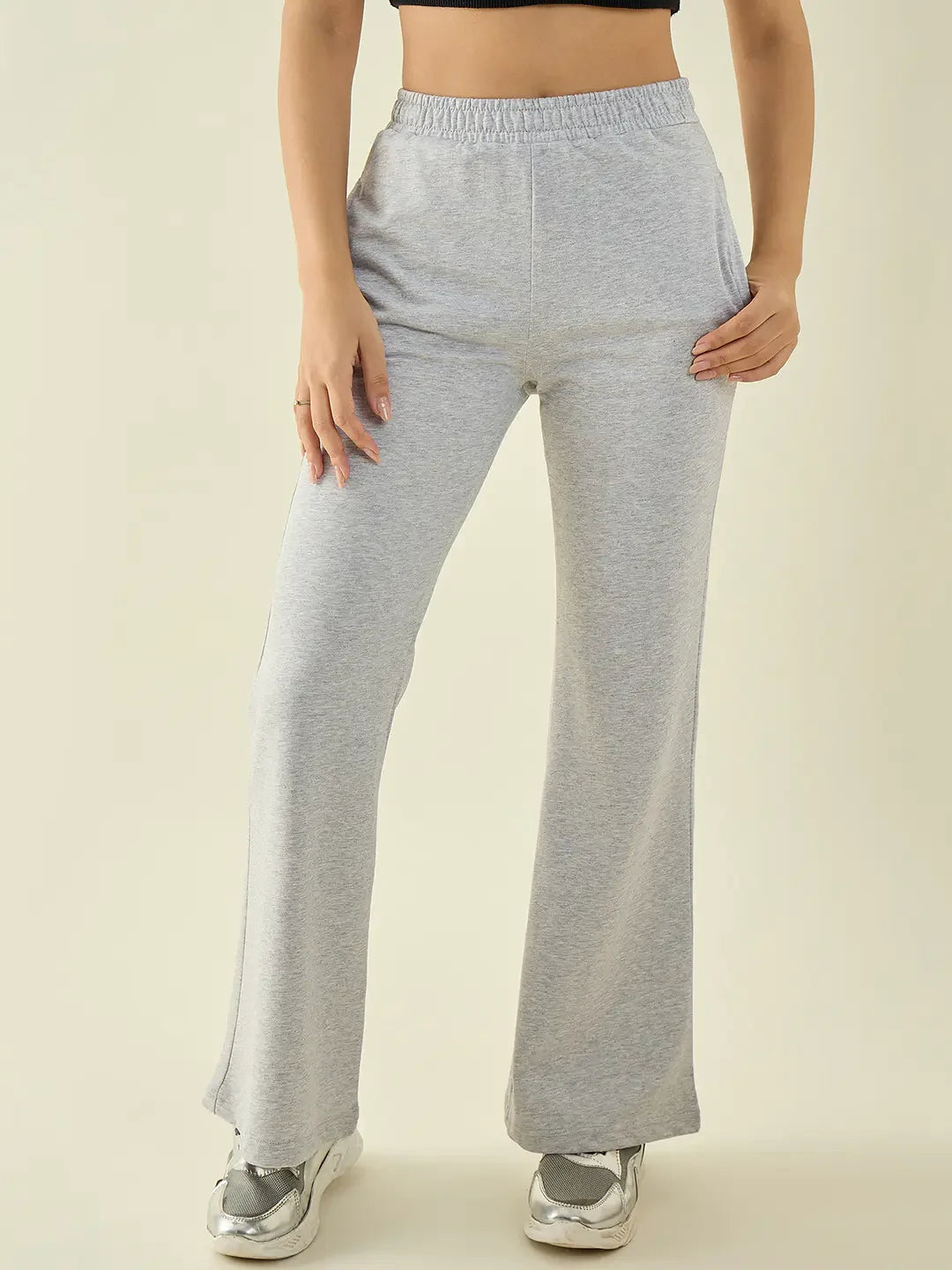 Woman in 98degreenorth light grey flared bootcut trousers, black crop top & silver sneakers, hands in pockets.