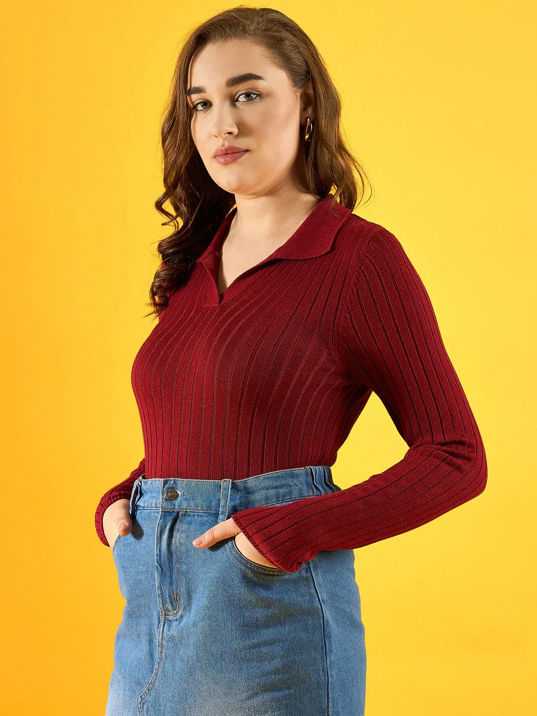 Woman in 98degreenorth maroon ribbed collar neck sweater and blue jeans stands against a yellow background.