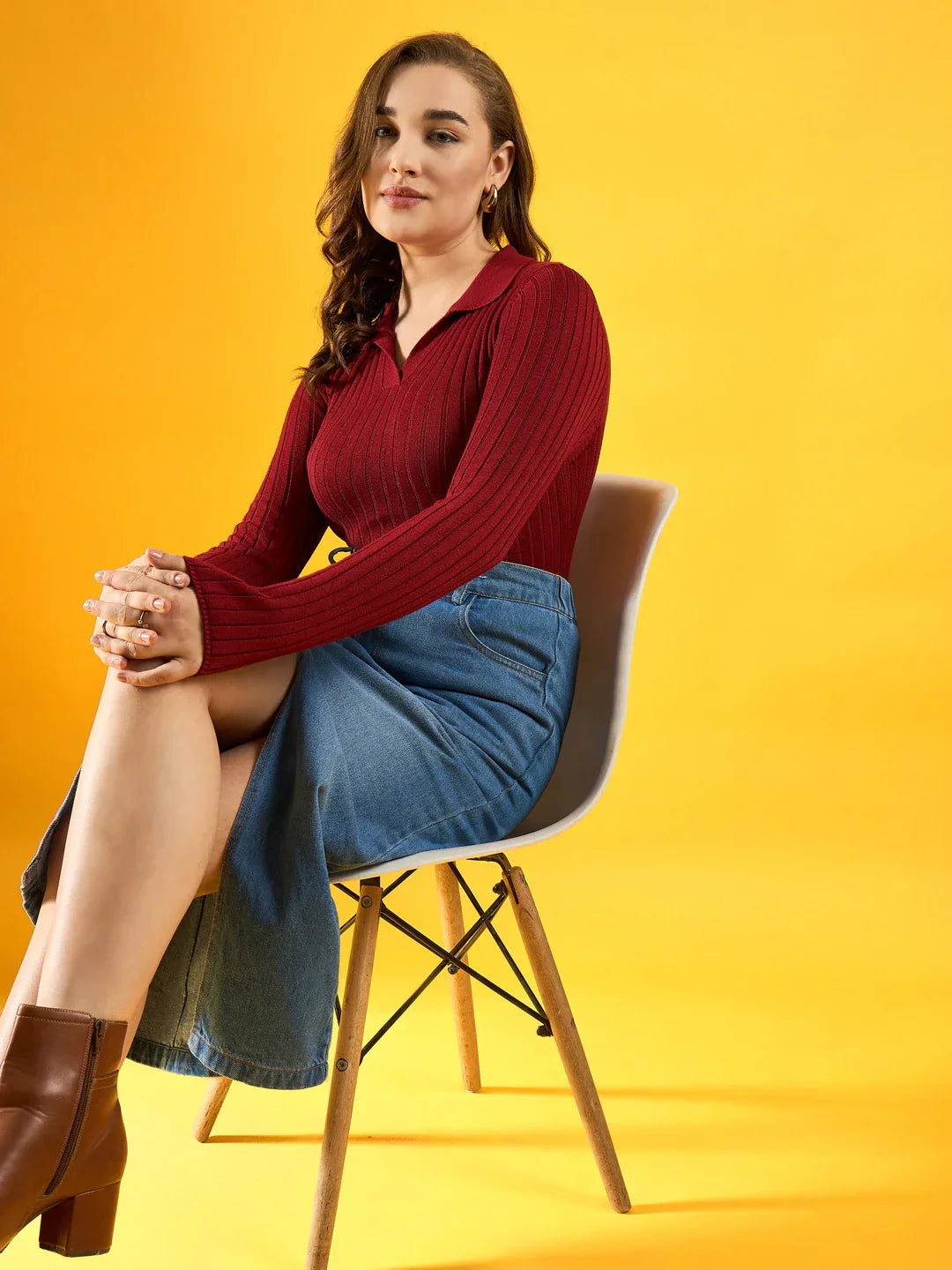 Woman wears 98degreenorth’s maroon ribbed collar neck slim fit sweater paired with a denim skirt, seated on a yellow backdrop.
