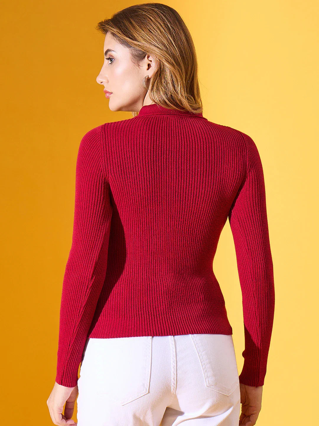 Woman in a 98degreenorth maroon ribbed collar zipper sweater and white pants stands against a yellow background.
