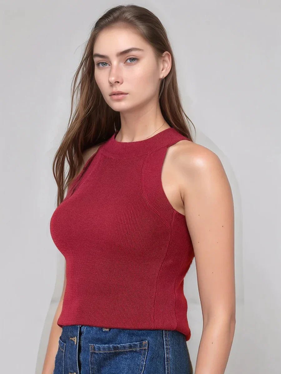 Woman with long brown hair in a 98degreenorth maroon ribbed halter neck sleeveless knit top and blue jeans against a gray backdrop.