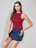 A woman in a 98degreenorth maroon ribbed halter neck slim fit knit top and denim mini skirt poses by a gray backdrop.