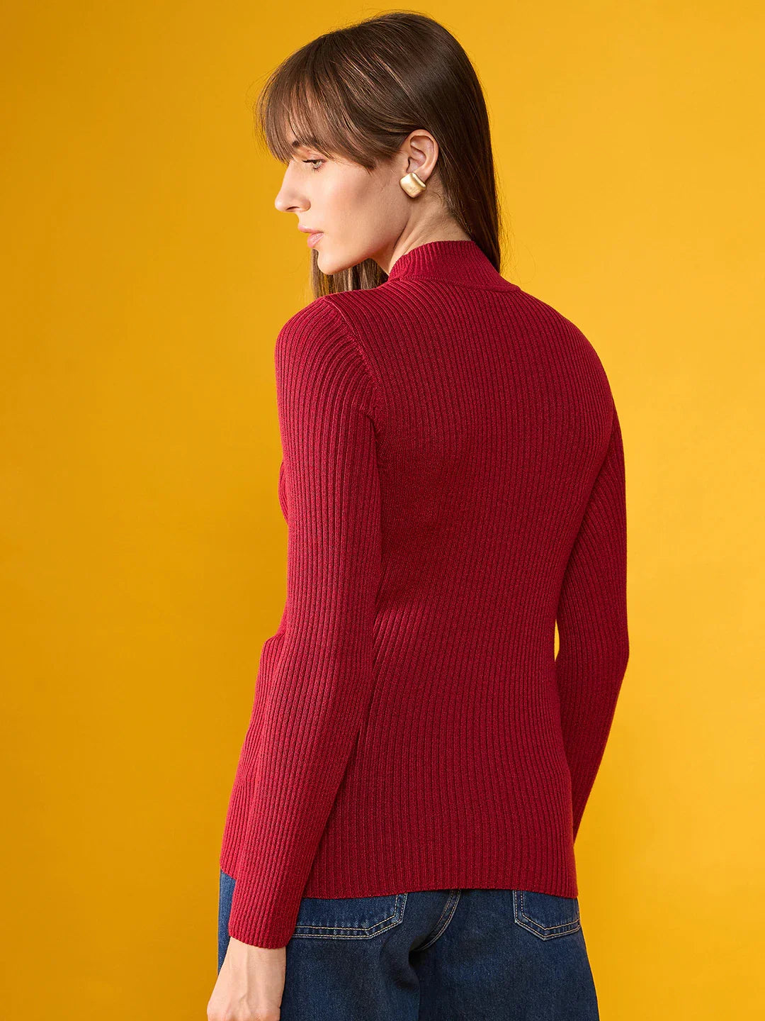 Woman in a 98degreenorth maroon ribbed turtleneck slim fit sweater and blue jeans, facing away, on yellow background.