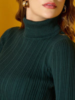 A woman in a 98degreenorth military green ribbed turtleneck sweater and gold hoops, with wavy hair and pink lipstick.