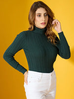 Woman in a 98degreenorth military green ribbed turtleneck sweater and white pants poses against a yellow background.