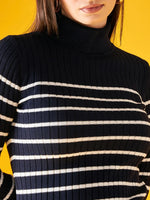 Woman in a 98degreenorth navy blue striped ribbed turtleneck sweater stands against a yellow background.