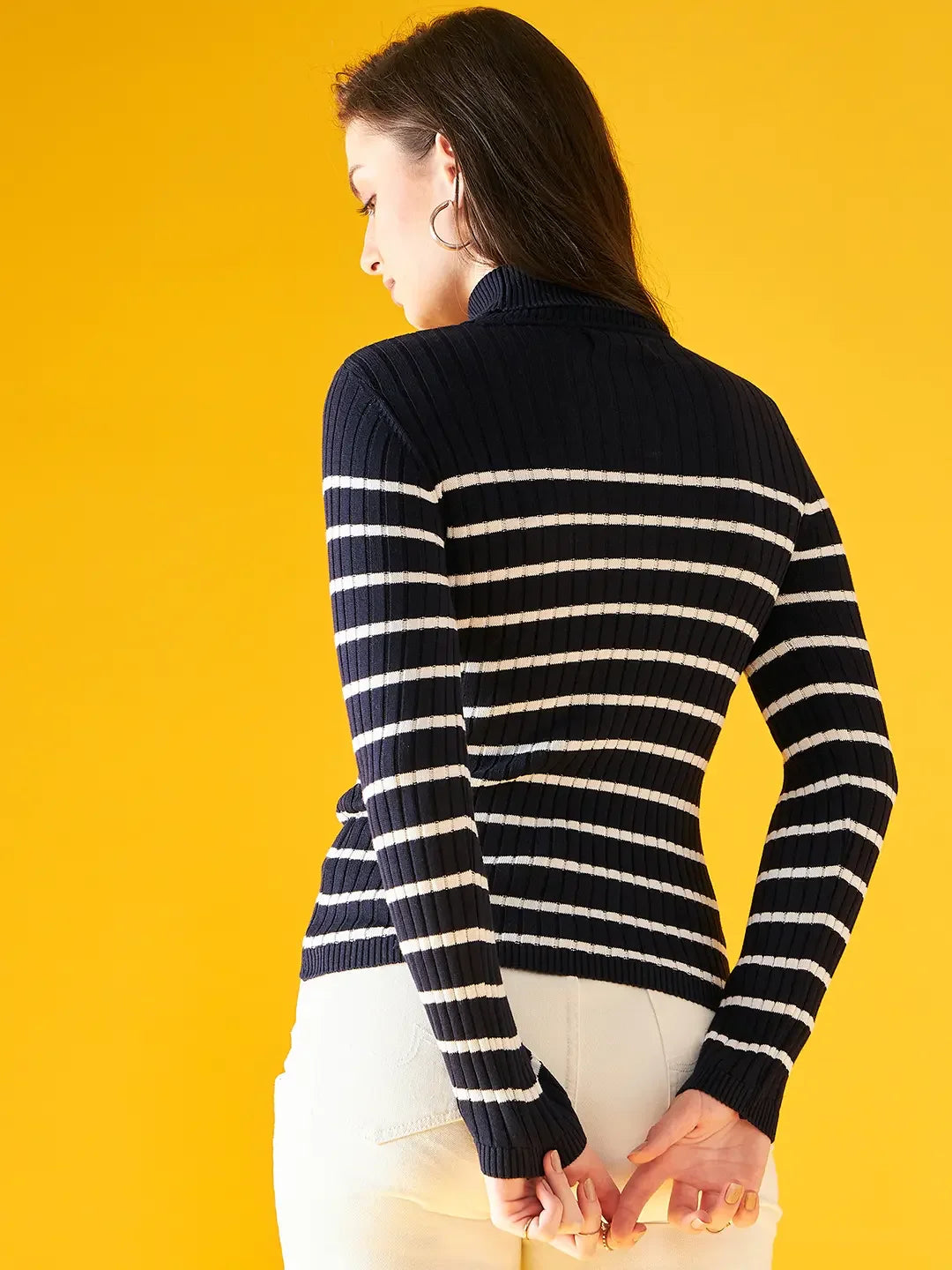 Woman in a 98degreenorth Navy Blue Striped Ribbed Turtleneck Sweater stands against a yellow background, facing away.