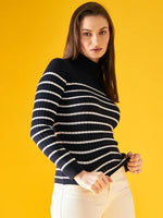 Woman wears 98degreenorth Women’s Navy Blue Striped Ribbed Turtleneck Sweater with white pants on a yellow backdrop.