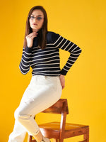 A woman wears a 98degreenorth navy striped turtleneck sweater, posing confidently on a chair with a yellow backdrop.