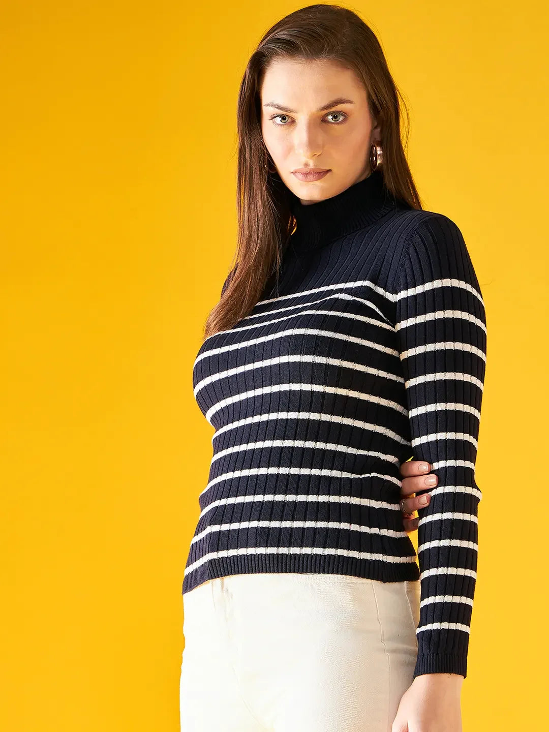 Woman wears a 98degreenorth navy blue striped ribbed turtleneck sweater, posing before a bright yellow background.