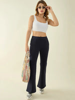 Woman in a white crop top and 98degreenorth navy flared bootcut trousers, sunglasses, sneakers, holding a tote bag.