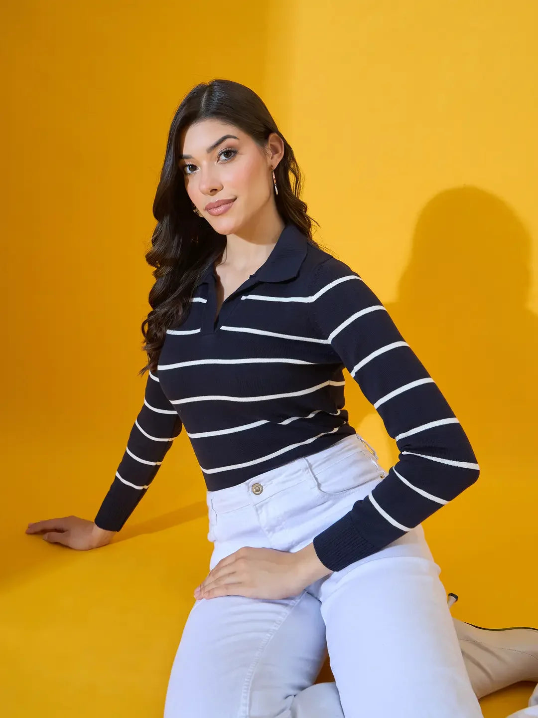 Woman wears 98degreenorth Women’s Navy Striped Collared Knit Sweater against a yellow background.