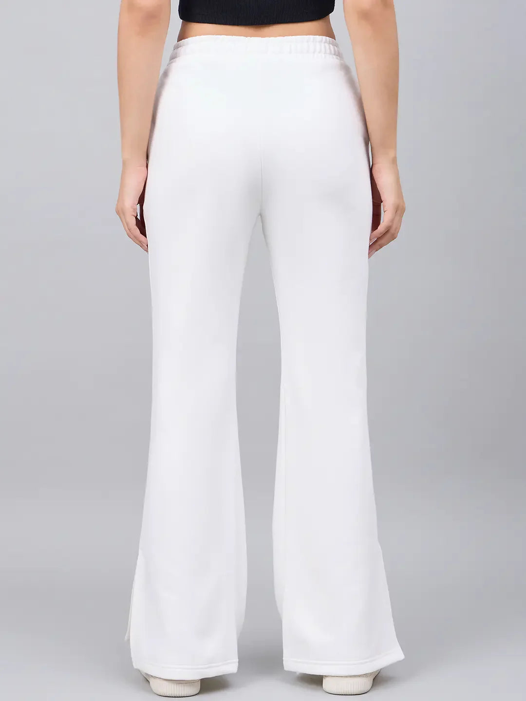 Woman in 98degreenorth off-white bootcut sweatpants, flared high-waist with side slit, seen from the back on gray.