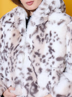 Woman in a 98degreenorth Off-White Faux Fur Jacket stands against a vibrant yellow background.
