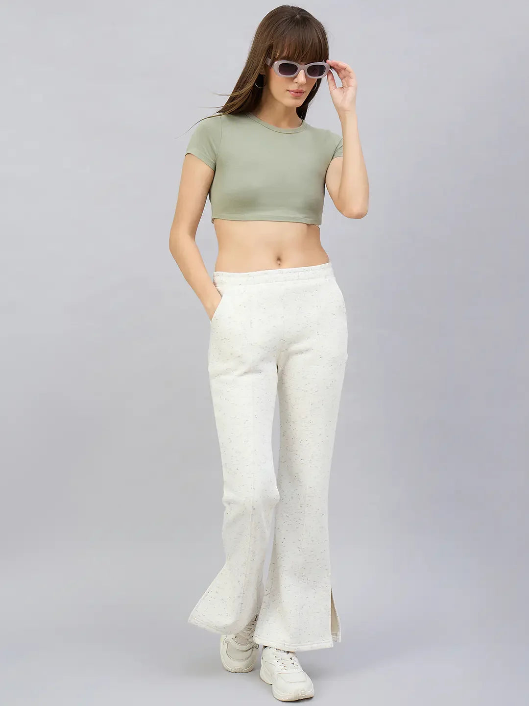 Woman in off-white 98degreenorth bootcut sweatpants with side slits and a green crop top stands with sunglasses.