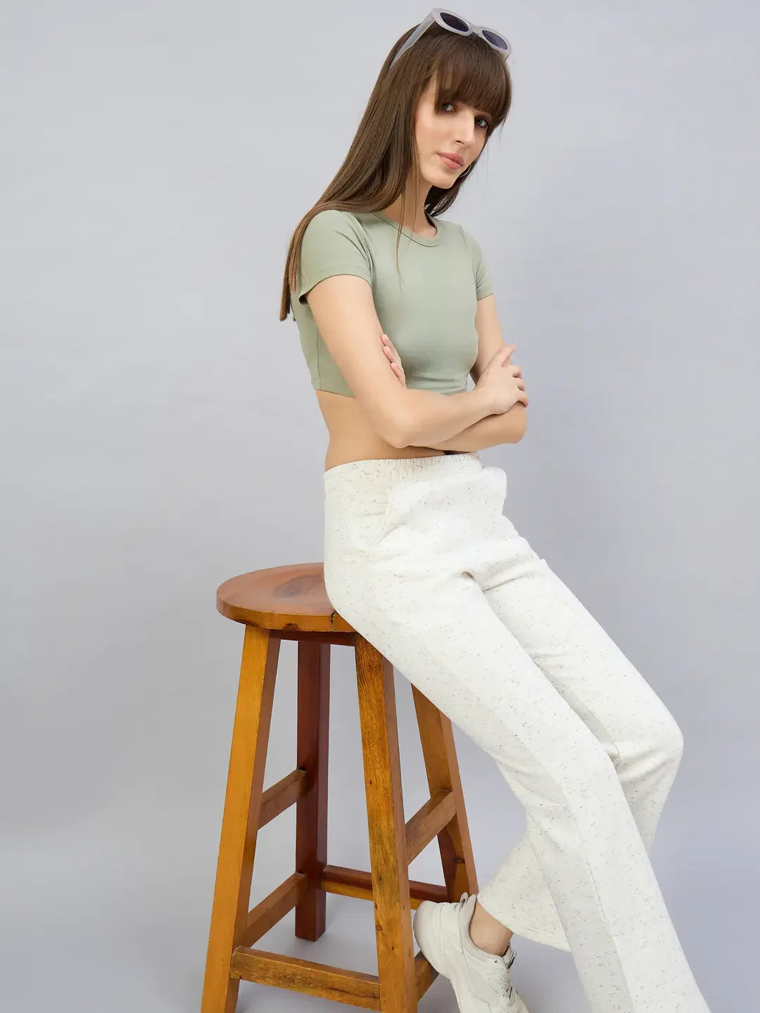 Woman models 98degreenorth off-white hairy texture bootcut sweatpants with side slits, sitting on a wooden stool.
