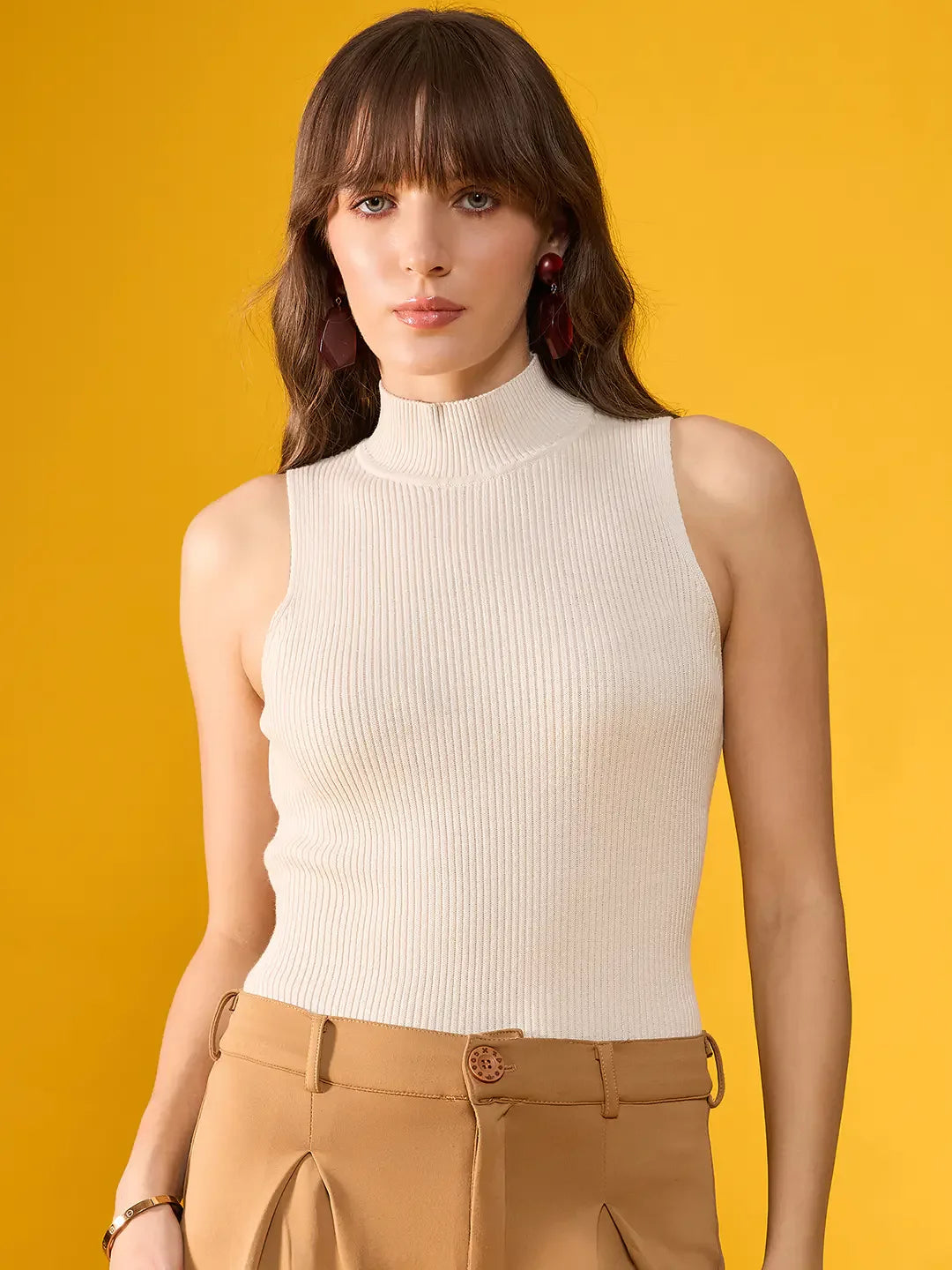Woman with long brown hair in a 98degreenorth off-white ribbed high neck sleeveless knit top, against a yellow background.