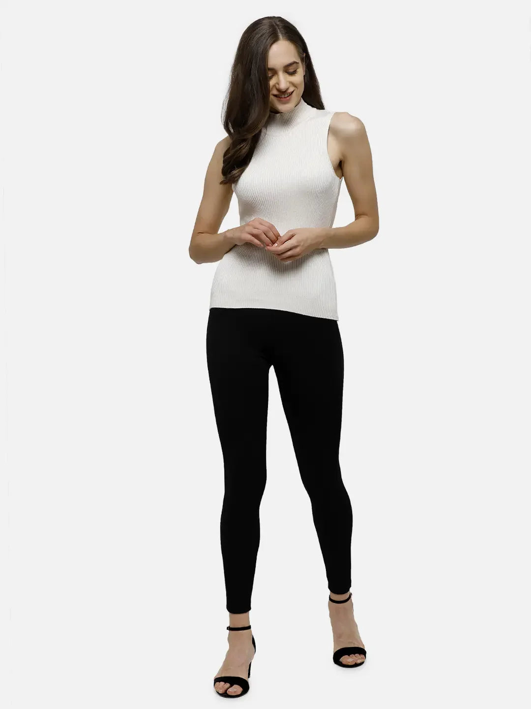 Woman wearing 98degreenorth Off-White Ribbed High Neck Sleeveless Knit Top, black leggings, and sandals, smiling.